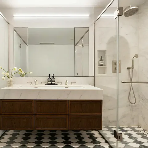 Primary bathroom with a walnut double vanity, marble walls and a glass shower over patterned marble floor tile at Midtown Luxury Residences, 30 East 31 Street, New York City, interior design by Alexandra Peck Design