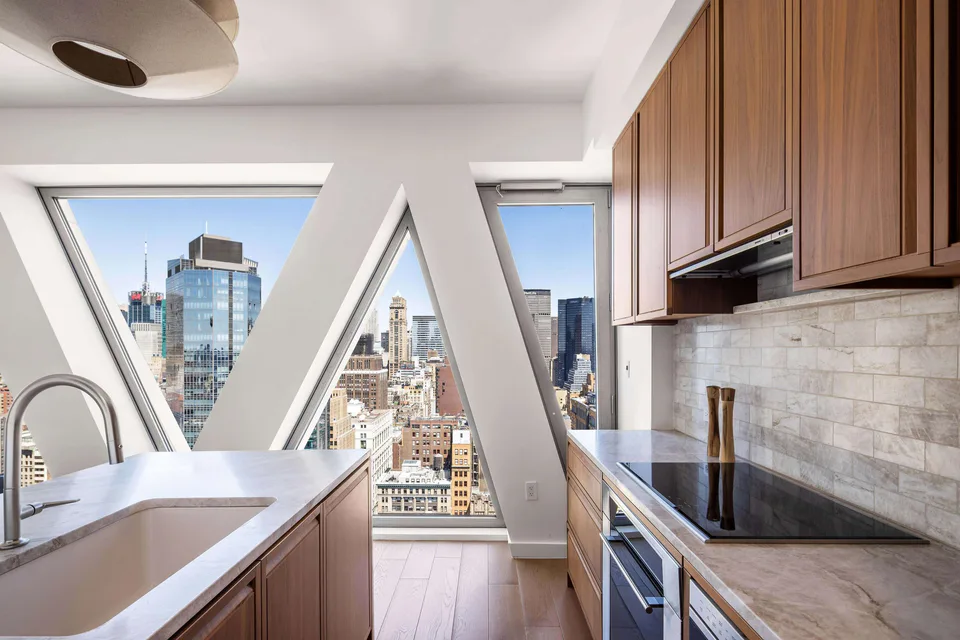 Kitchen with walnut cabinetry and quartzite counters before the facade’s diagonal lattice windows over Midtown at Midtown Luxury Residences, 30 East 31 Street, New York City, interior design by Alexandra Peck Design