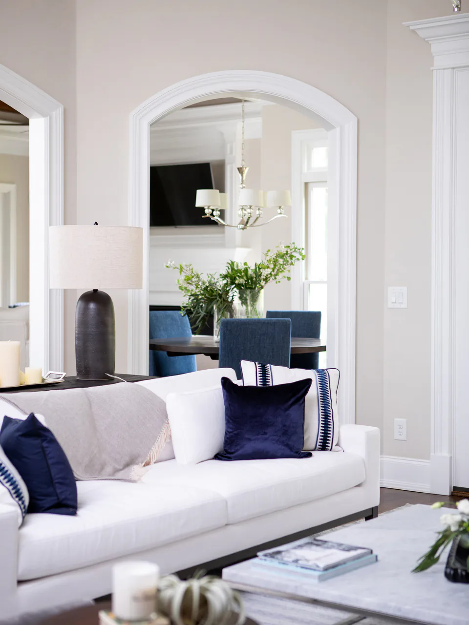 Living room with a white linen sofa, navy velvet and banded pillows and an arched doorway to the breakfast room at Durham Transitional, Durham, North Carolina, interior design by Alexandra Peck Design