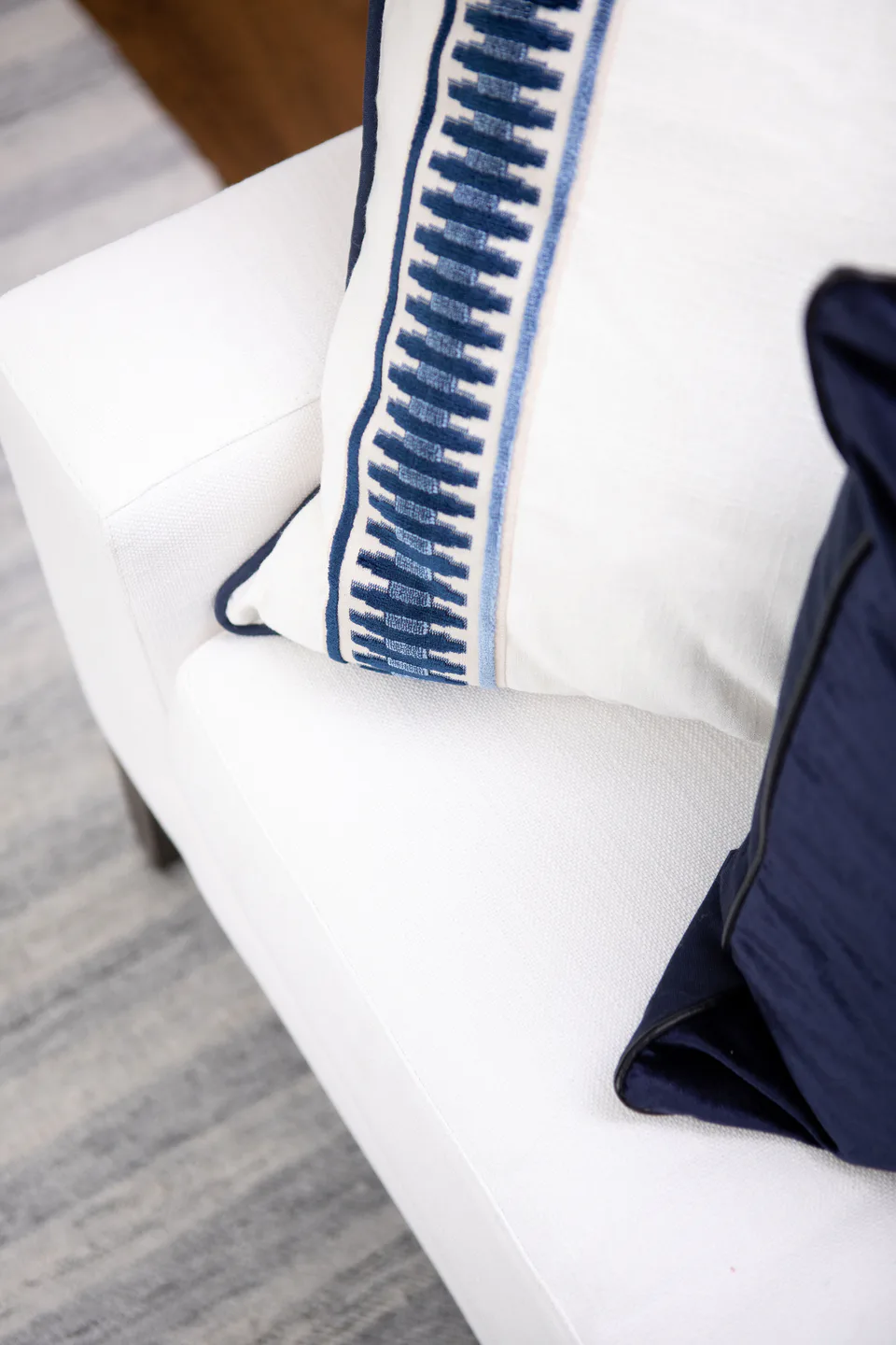 Hand-stitched satin-banded throw pillow with blue embroidery and a navy velvet pillow on the white linen sofa in the living room at Durham Transitional, Durham, North Carolina, interior design by Alexandra Peck Design