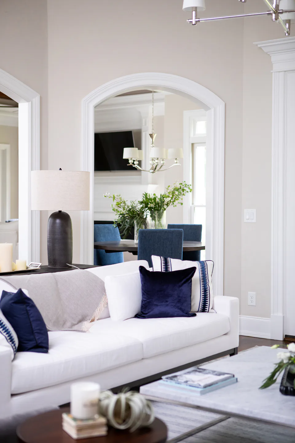 White linen sofa with navy velvet and banded pillows, an arched doorway to the breakfast room beyond at Durham Transitional, Durham, North Carolina, interior design by Alexandra Peck Design