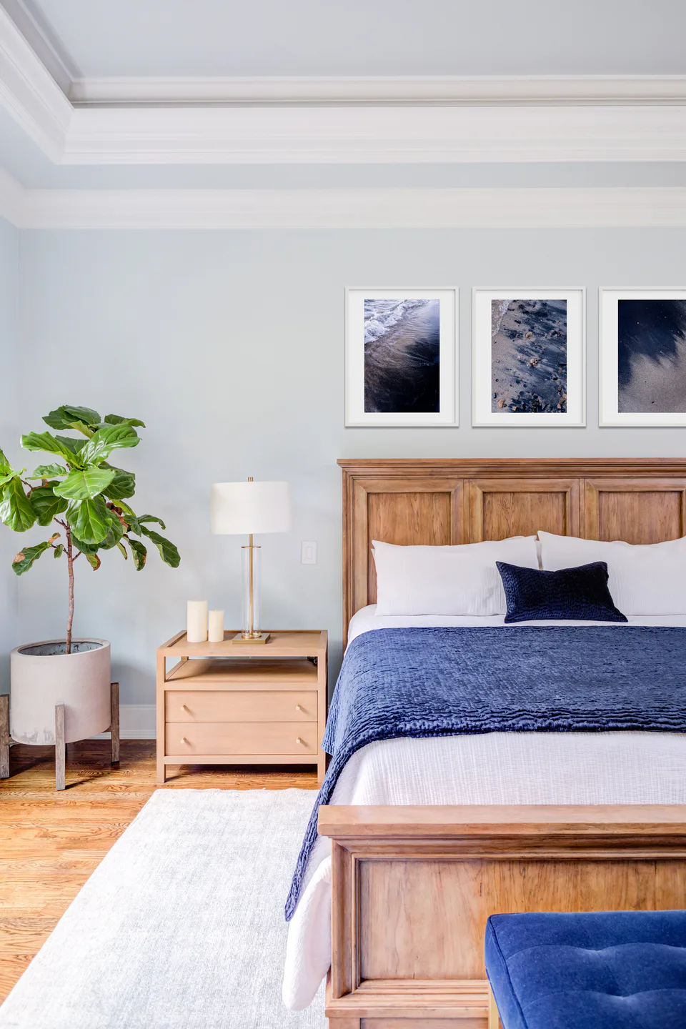 Main bedroom with a wood bed dressed in white bedding and a deep blue velvet throw, a fiddle-leaf fig and three framed prints at Durham Transitional, Durham, North Carolina, interior design by Alexandra Peck Design