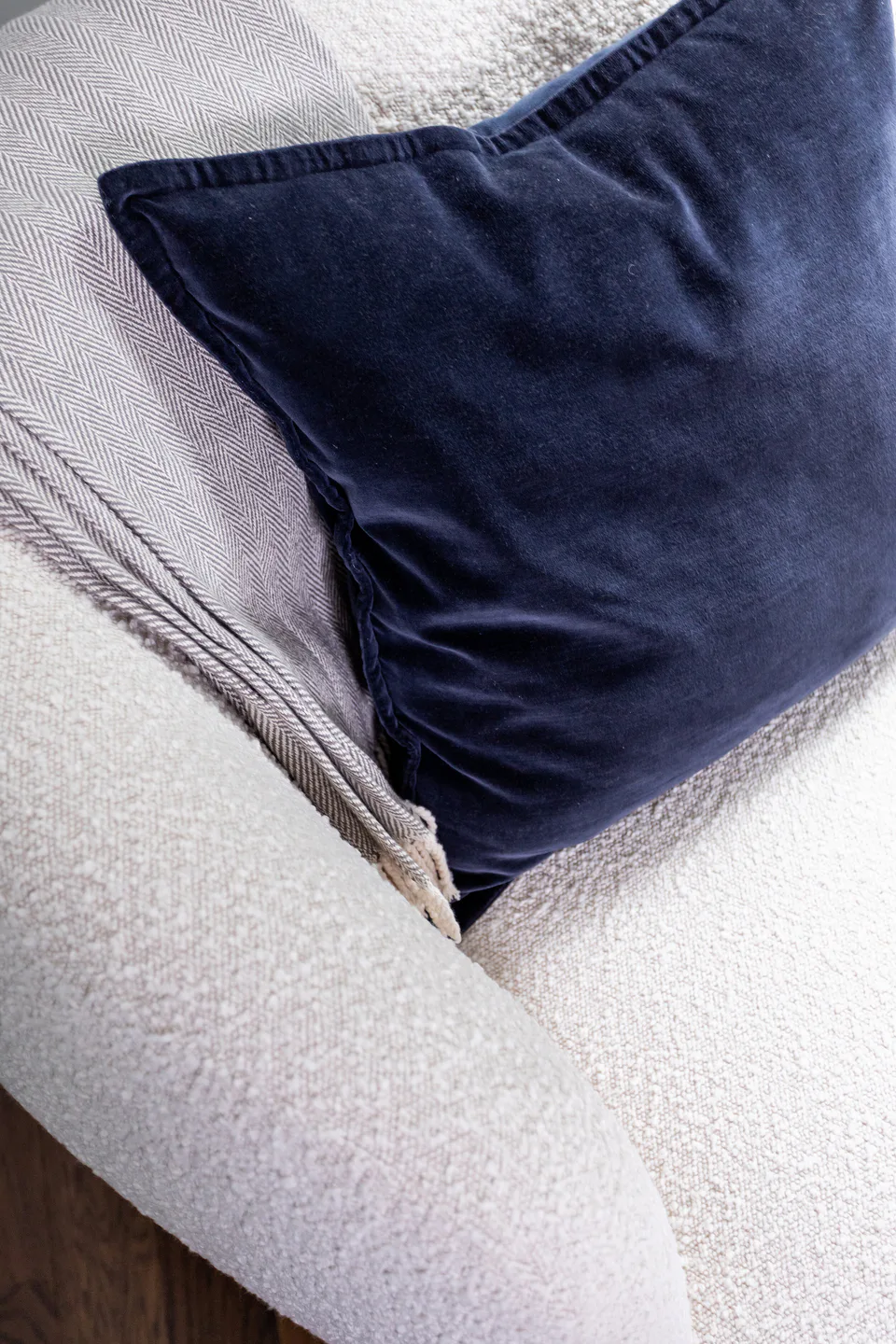 Deep blue velvet throw pillow and gray herringbone wool blanket on an off-white bouclé swivel lounge chair in the main bedroom at Durham Transitional, Durham, North Carolina, interior design by Alexandra Peck Design