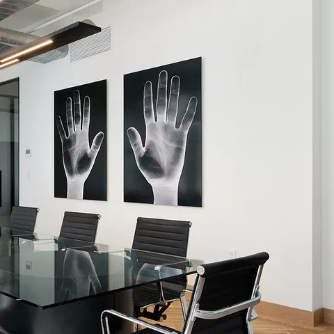 Detail: two framed hand photographs above the black glass table and leather task chairs in the conference room at Flatiron Workplace, 3 East 28th Street, New York City, interior design by Alexandra Peck Design
