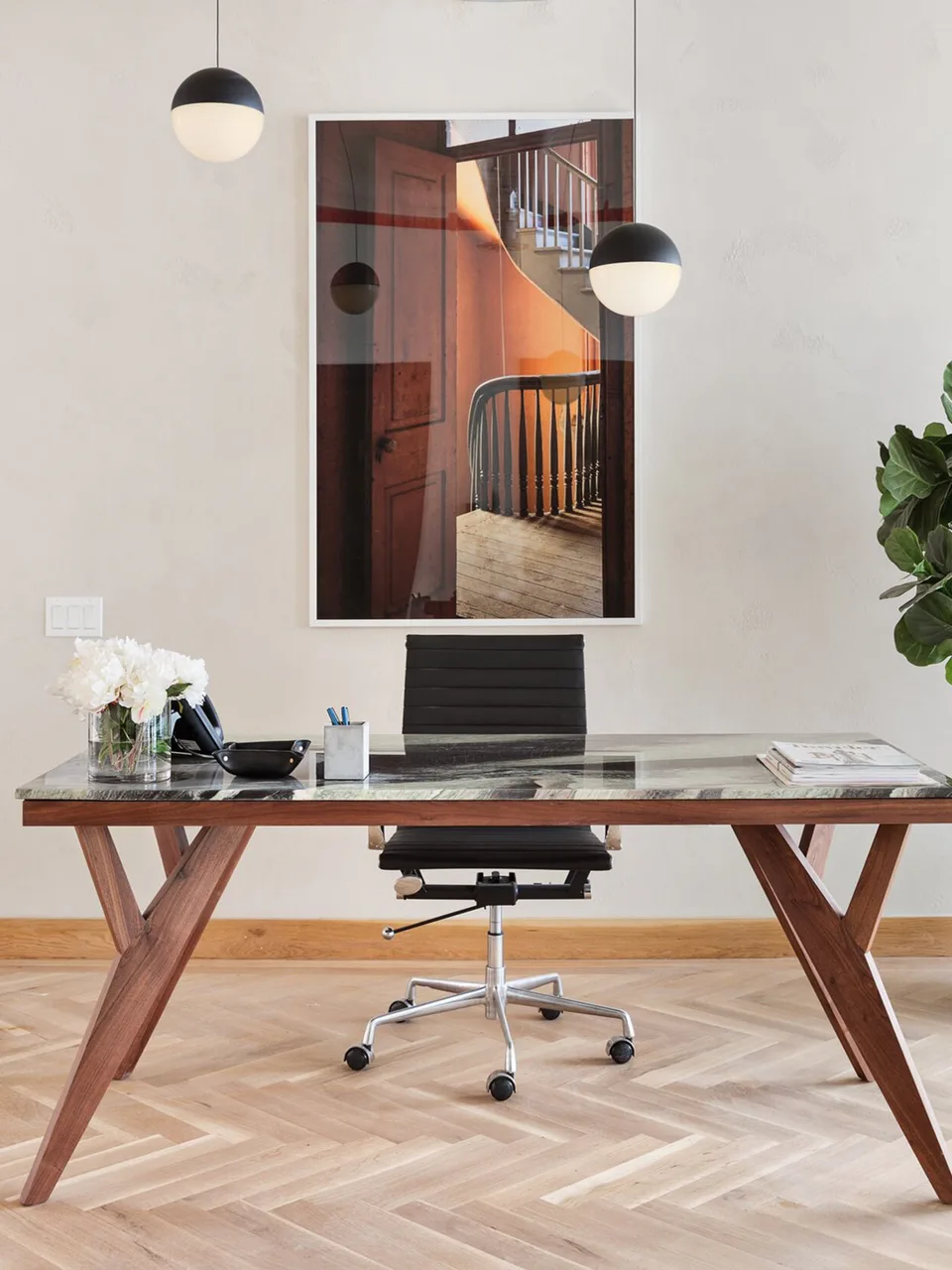 Reception desk in walnut and glass with a black leather chair, globe pendants and a framed photograph on herringbone oak floors at Flatiron Workplace, 3 East 28th Street, New York City, interior design by Alexandra Peck Design