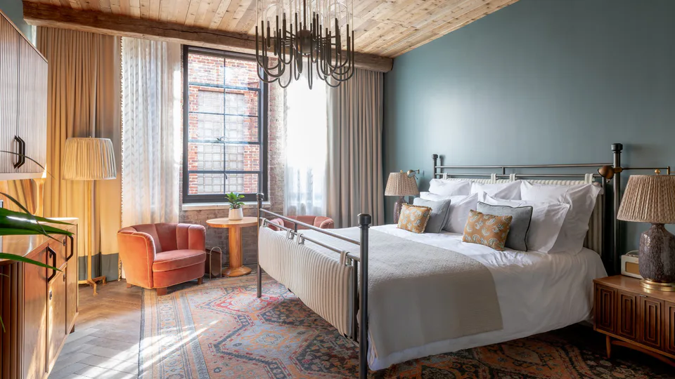Medium bedroom with an iron bed, a sculptural chandelier, a timber ceiling and blue walls at Soho House Nashville, Nashville, Tennessee, interior design by Alexandra Peck Design
