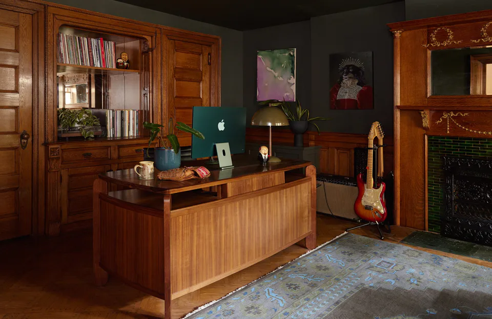 Moss-green study with a mid-century walnut desk, built-in bookcase, electric guitar and emerald-tiled fireplace, with artwork by Peter Calvin and Jenny C’est Quoi, at the Prospect Heights Brownstone, Brooklyn, New York, interior design by Alexandra Peck Design