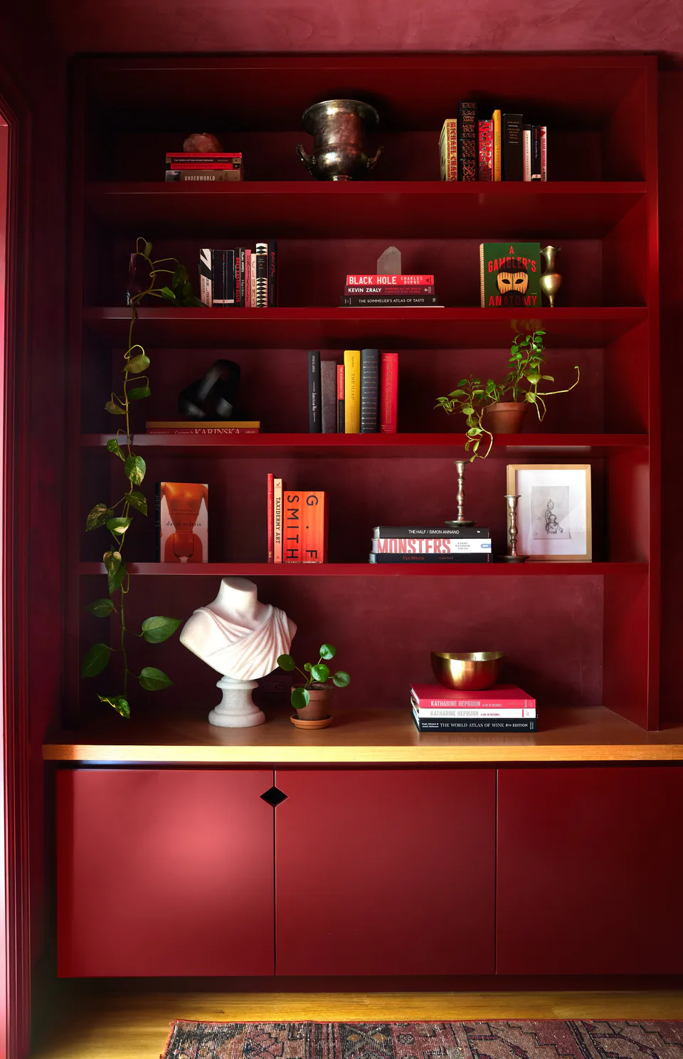 Lacquered burgundy built-in shelves displaying novels, a classical bust and travel mementos in the library at the Prospect Heights Brownstone, Brooklyn, New York, interior design by Alexandra Peck Design