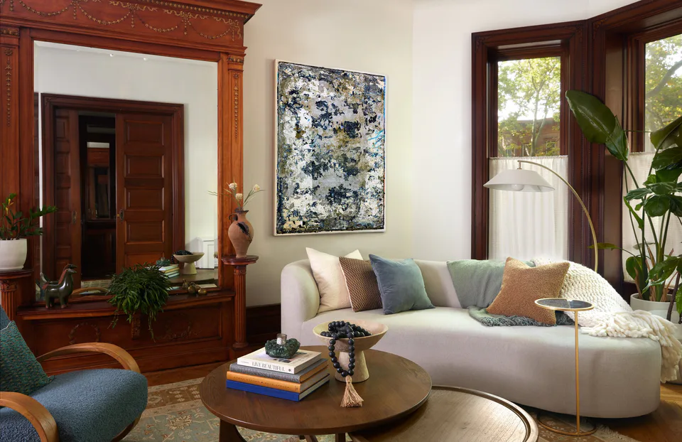 Parlor living room with a curved sofa, restored built-in mirror and original artwork beside the bay windows at the Prospect Heights Brownstone, Brooklyn, New York, interior design by Alexandra Peck Design