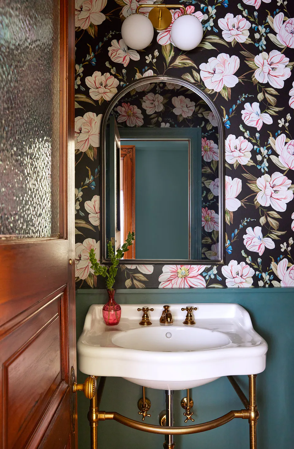 Jewel box powder room with a bold floral wallcovering, an arched mirror and a console sink on brass legs at the Prospect Heights Brownstone, Brooklyn, New York, interior design by Alexandra Peck Design