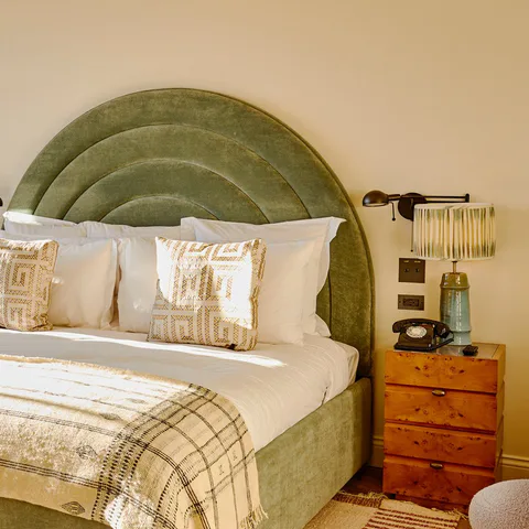 Detail: arched green velvet headboard, a pleated wall light and a burl bedside chest in a small bedroom at Soho House Nashville, Nashville, Tennessee, interior design by Alexandra Peck Design