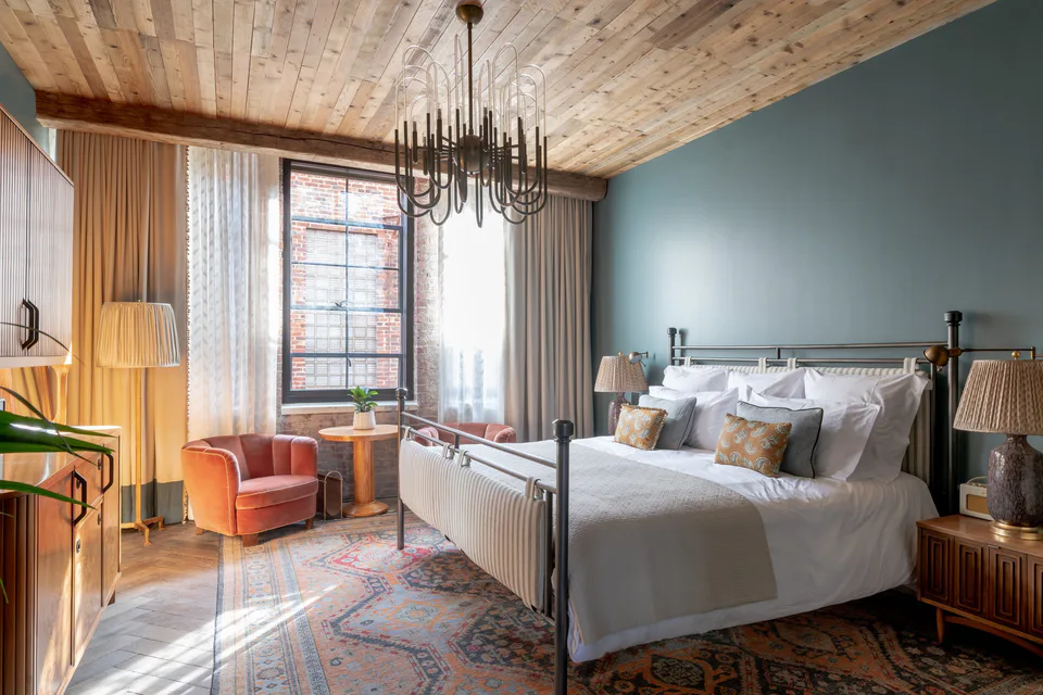 Medium bedroom with an iron bed, a sculptural chandelier, a timber ceiling and blue walls at Soho House Nashville, Nashville, Tennessee, interior design by Alexandra Peck Design