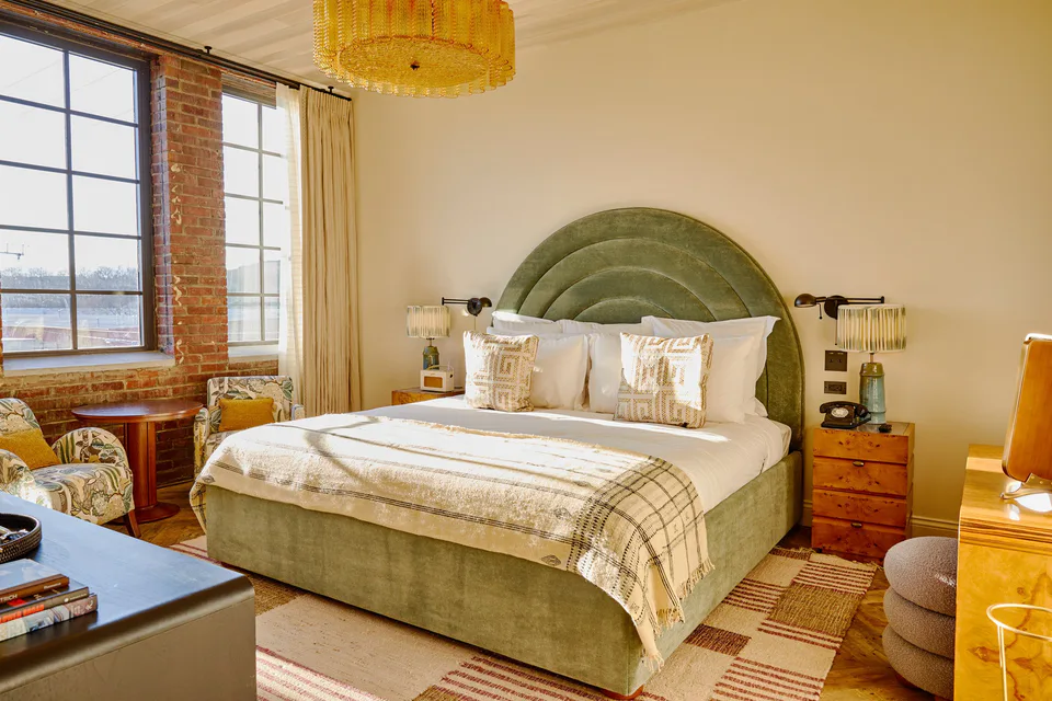 Small bedroom with an arched green velvet headboard, a plaid throw and factory windows at Soho House Nashville, Nashville, Tennessee, interior design by Alexandra Peck Design