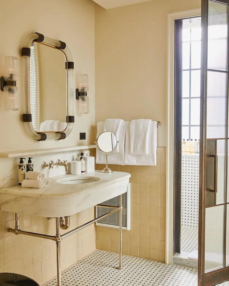 Small bedroom bathroom with a console sink, an oval mirror with sconces and pale yellow tiles at Soho House Nashville, Nashville, Tennessee, interior design by Alexandra Peck Design