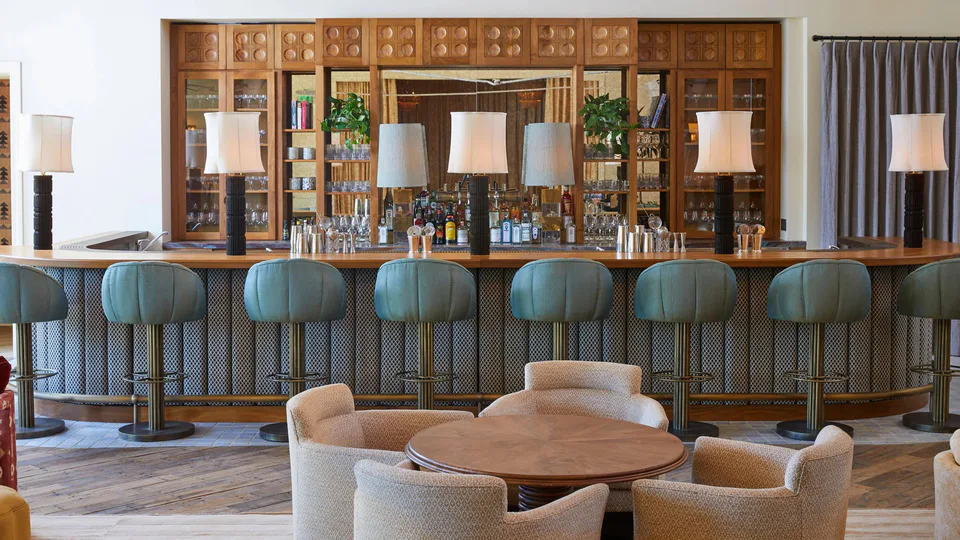 The Sock Room bar with teal bar stools, table lamps along the counter and a timber back bar at Soho House Nashville, Nashville, Tennessee, interior design by Alexandra Peck Design