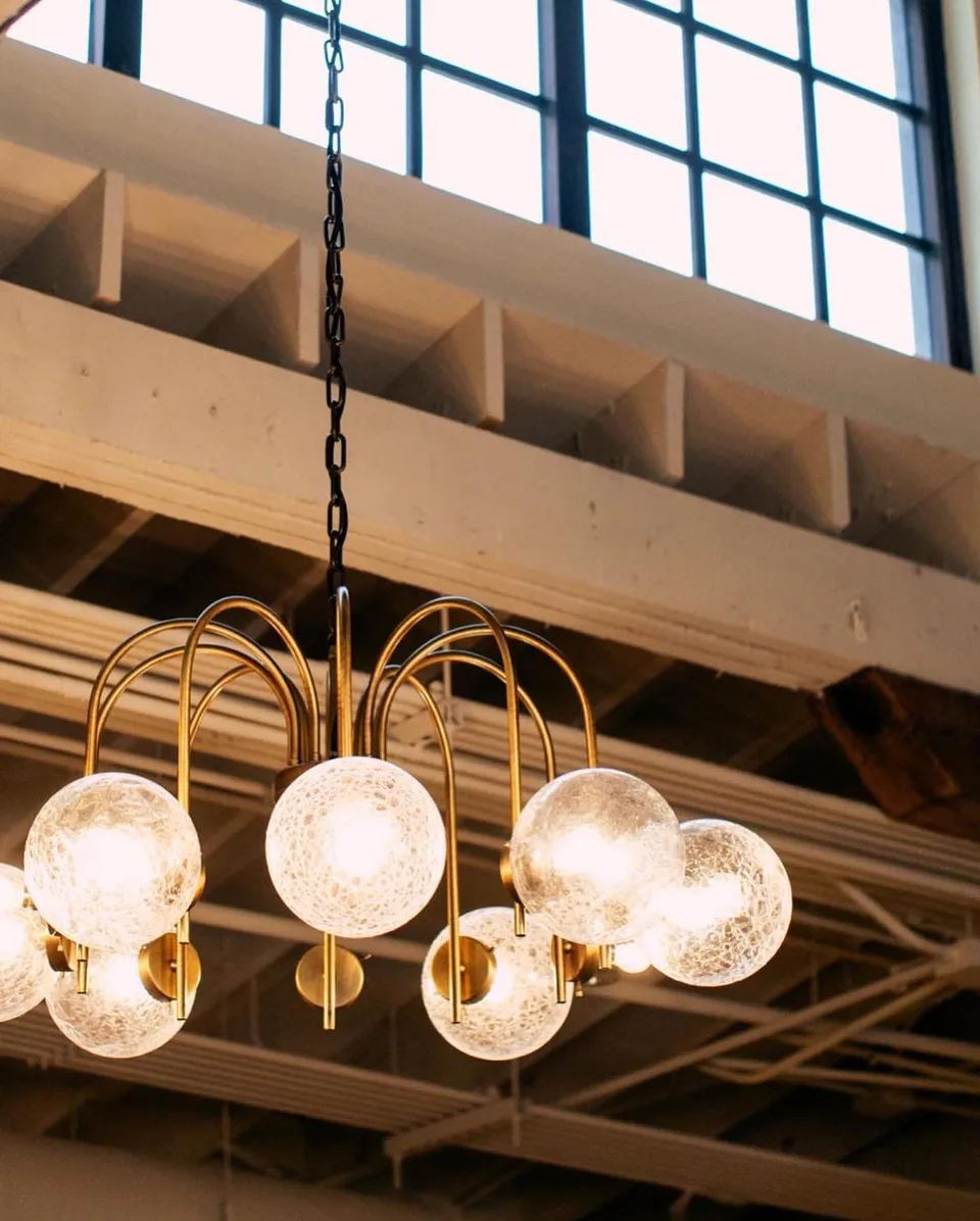 Brass chandelier with frosted glass globes beneath the factory ceiling in The Sock Room at Soho House Nashville, Nashville, Tennessee, interior design by Alexandra Peck Design