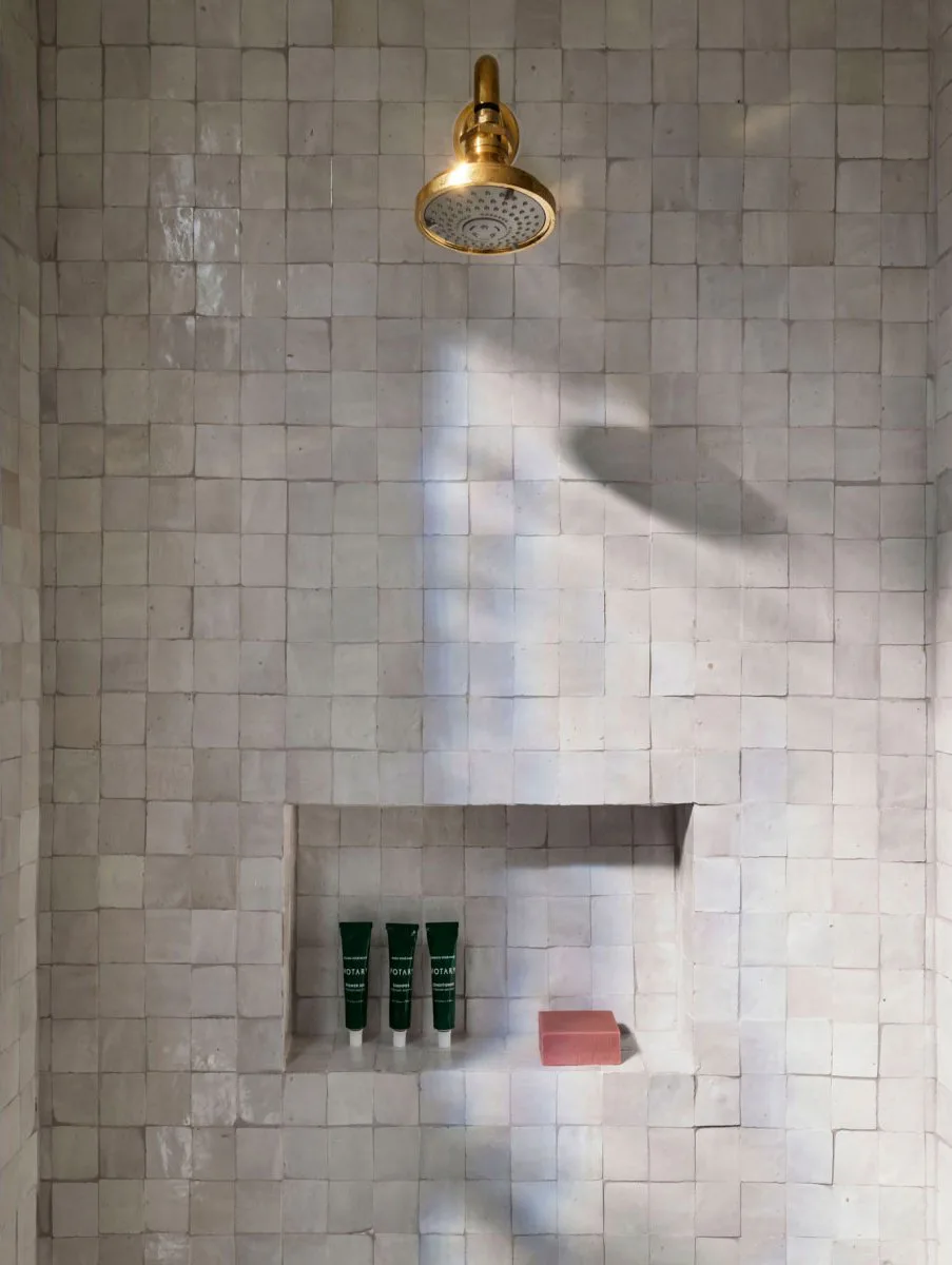 White glazed zellige tile shower with a brass shower head and a niche at The Pinch Hotel, Charleston, South Carolina, interior design by Alexandra Peck Design