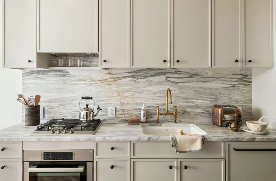 Guest kitchen with Shaker cabinetry, a marble backsplash and a brass bridge faucet at The Pinch Hotel, Charleston, South Carolina, interior design by Alexandra Peck Design