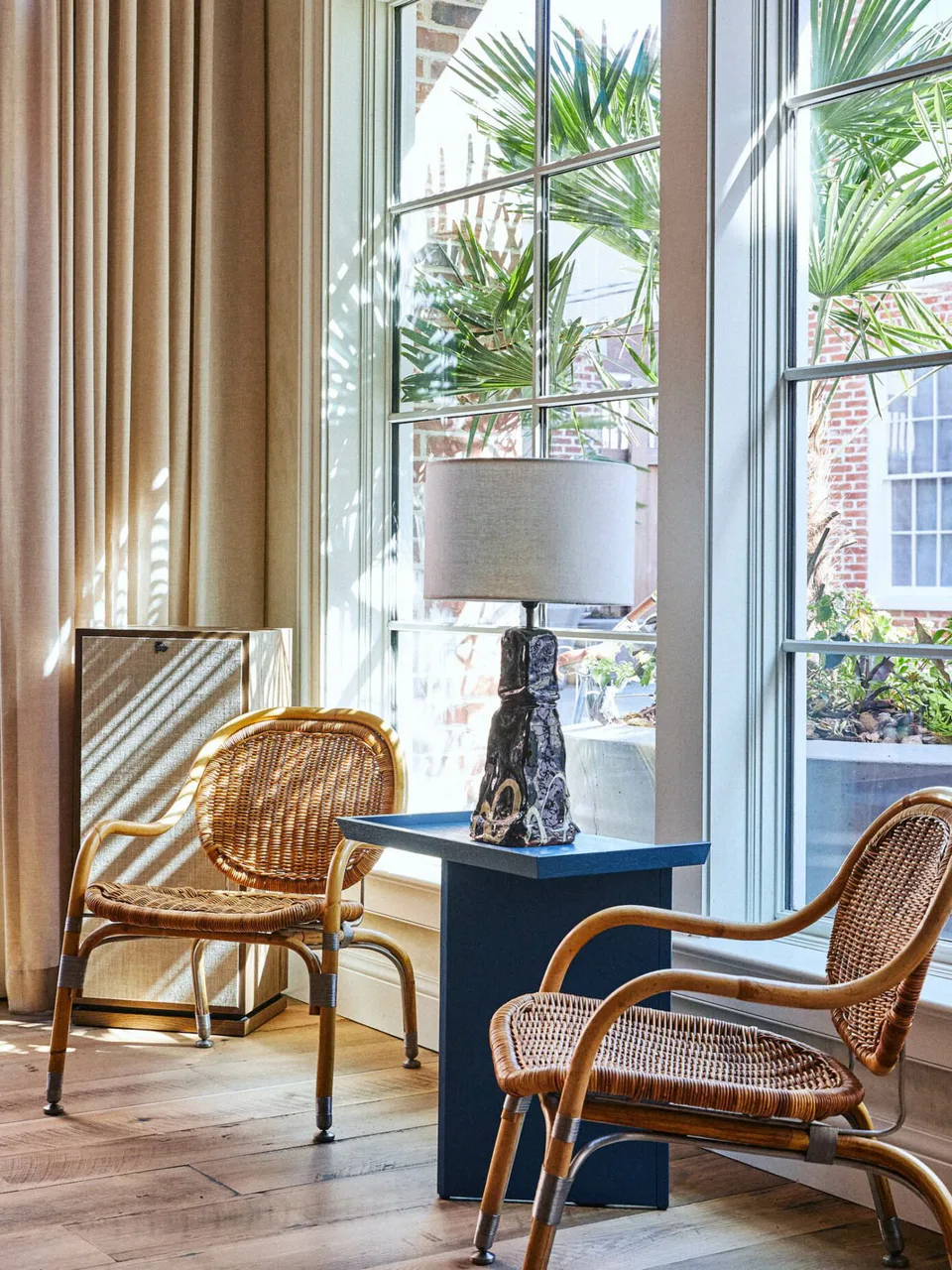 Rattan armchairs and a blue side table with a sculptural lamp by the tall lobby windows at The Pinch Hotel, Charleston, South Carolina, interior design by Alexandra Peck Design
