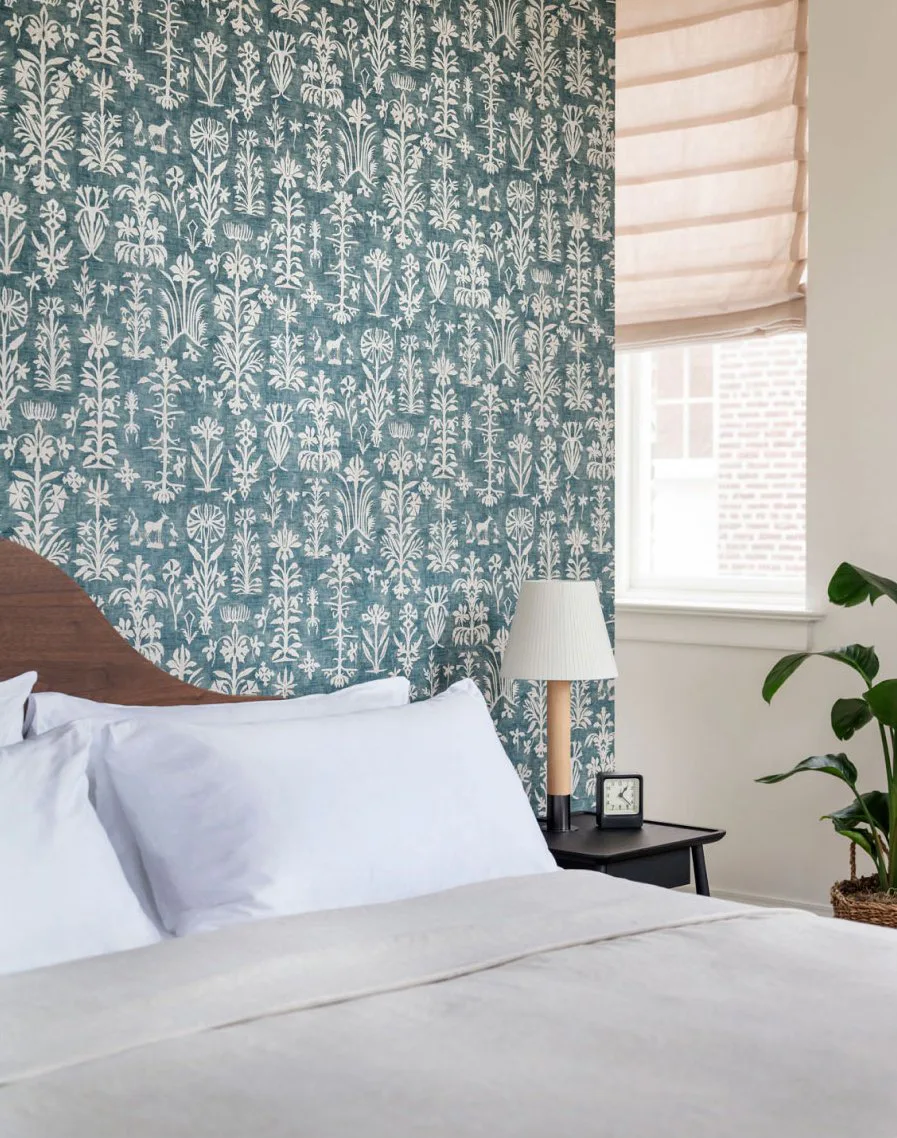 Suite bedroom with a patterned teal wallpaper, a curved wooden headboard and white linen at The Pinch Hotel, Charleston, South Carolina, interior design by Alexandra Peck Design