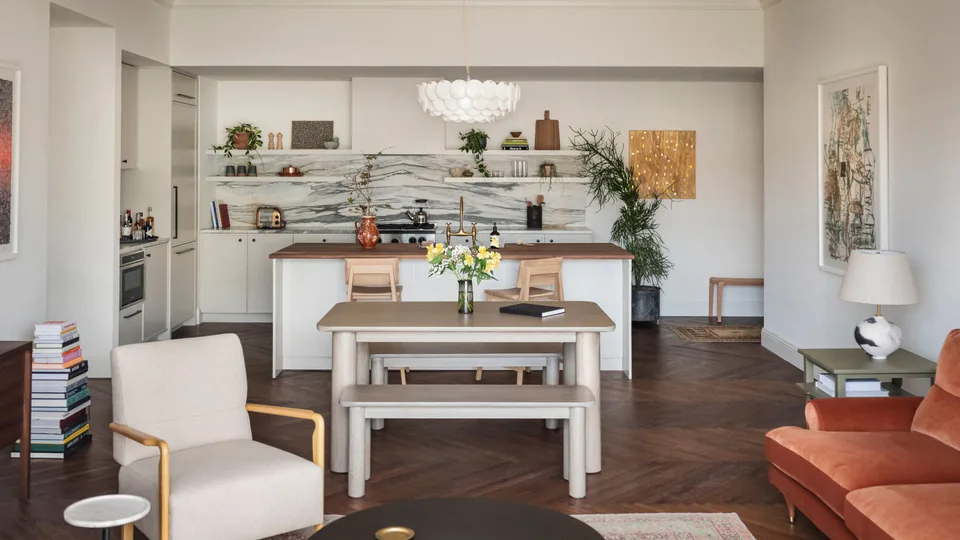 Open-plan suite with a long dining table and benches beneath a white pendant, the kitchen beyond, at The Pinch Hotel, Charleston, South Carolina, interior design by Alexandra Peck Design
